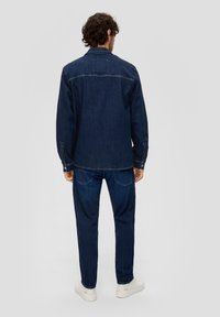 Donkerdenim jasje en broekset, met een klassieke uitstraling, knoopdetails en een zachte textuur, gecombineerd met witte sneakers.
