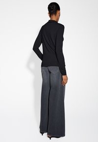 Schwarzes Langarmoberteil mit hohem Kragen, kombiniert mit weit geschnittenen, dunkelgrauen Jeans. Das Outfit zeichnet sich durch einen glatten Stoff und eine enganliegende Silhouette aus.