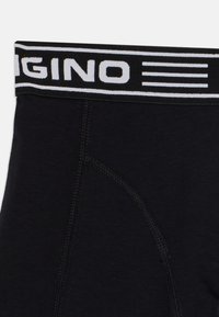 Schwarze Unterwäsche mit einem weißen, gebrandeten elastischen Bund und horizontalen Streifen. Der Stoff ist glatt und zeigt sichtbare Stickdetails.