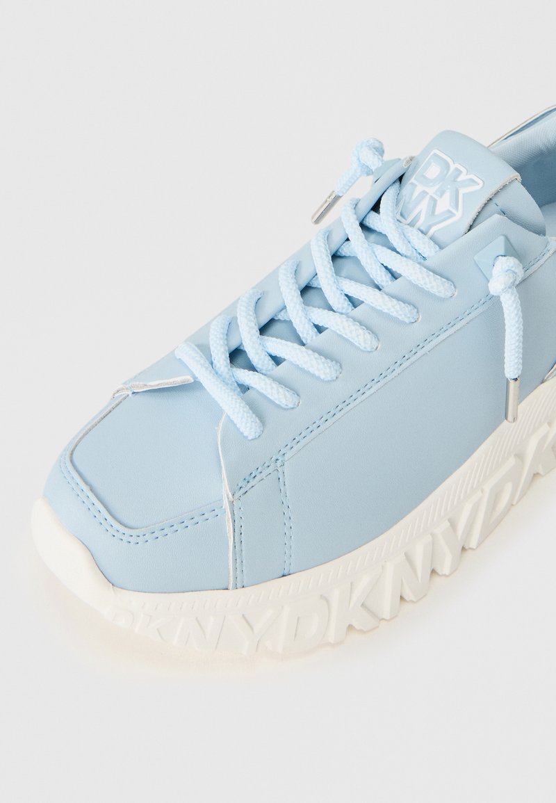 Sneaker azzurro chiaro con logo "DKNY" in rilievo bianco sulla suola, lacci coordinati e linguetta imbottita su uno sfondo bianco.