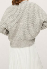 Vaaleanharmaa neulepaita, jossa on väljähkö istuvuus ja lasketut olkapäät. Resorireunus ja teksturoitu kuvio. Päällä valkoinen laskostettu hame.