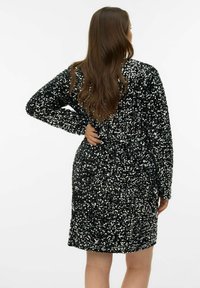 Robe noire couverte de sequins brillants, manches longues, longueur au genou, et coupe ample. Le dos est uni avec un léger éclat dû aux sequins.