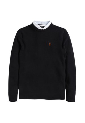 Schwarzer strukturiert gestrickter Pullover mit Rundhalsausschnitt, langen Ärmeln und kleinem orangefarbenem Hirschlogo auf der linken Brust, kombiniert mit einem weißen Hemd mit Kragen.