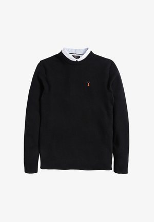 Schwarzer strukturiert gestrickter Pullover mit Rundhalsausschnitt, langen Ärmeln und kleinem orangefarbenem Hirschlogo auf der linken Brust, kombiniert mit einem weißen Hemd mit Kragen.