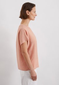 Haut rose clair à manches courtes avec une coupe décontractée et un col rond. Présente un tissu texturé et une légère variation de l'ourlet.