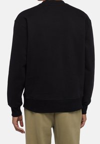 Svart sweatshirt med rund halsringning, sänkt axel och ribbade mudd och fåll. Tyget verkar mjukt och lätt texturerat.