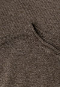 Gros plan sur un tissu de pull en maille marron montrant des coutures détaillées et le bord du col plié.