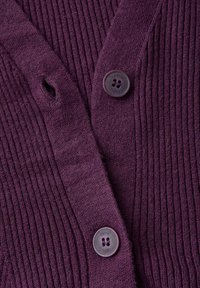 Lila gerippter Cardigan mit einem tiefen V-Ausschnitt und zwei runden Knöpfen mit vier Löchern, der aus einem weichen und strukturierten Stoff besteht.