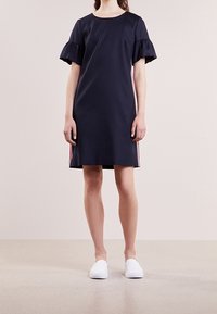 Robe courte marine à manches courtes avec volants, présentant des rayures verticales rouges et blanches sur les côtés. Tissu lisse, design à mi-mollet.