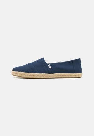 Navy canvas slip-on shoes with a jute rope sole, featuring a flat design and minimal stitching details.