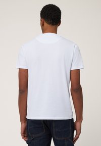 White cotton t-shirt with short sleeves, crew neckline, and a plain back. Paired with dark denim cargo pants featuring side pockets.