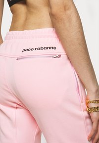 Ljusrosa joggers med elastisk midja, som har en svart "paco rabanne"-logotyp och en silverfärgad dragkedjeficka p å baksidan.