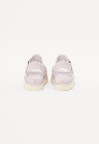 Vaaleanpunaiset mokkasiinit, joissa on teksturoitu pinta, avonainen takasuunnittelu, säätöremmit ja kermaiset kumipohjat, joissa on UGG-logo painettuna.