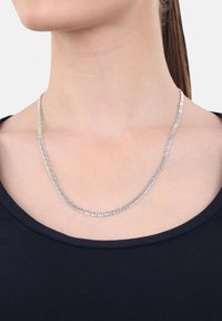 Collana in argento con link intricati indossata su un collo nudo sopra un top nero a girocollo, capelli raccolti.