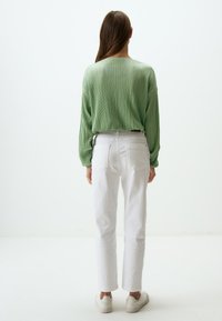 Blusa verde plissettata a maniche lunghe abbinata a jeans bianchi a gamba dritta e sneakers di colore chiaro, vista da dietro.