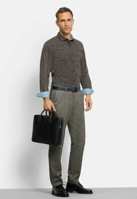 Herrenoutfit mit einem gemusterten dunklen Hemd mit Jeansmanschetten, grauen strukturierten Hosen, schwarzen Lederschuhen und einer schwarzen Aktentasche.