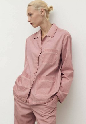 Chemise boutonnière rose clair avec deux poches avant, fabriquée en tissu doux. Dispose d'un col classique et d'une coupe décontractée. Texture lisse.