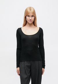 Μαύρο τοπ με μακριά μανίκια και φαρδύ ντεκολτέ σε σχήμα σέσουλας. Απαλή, λεία υφή με εφαρμοστή γραμμή, συνδυασμένο με φαρδιά γκρι παντελόνια.