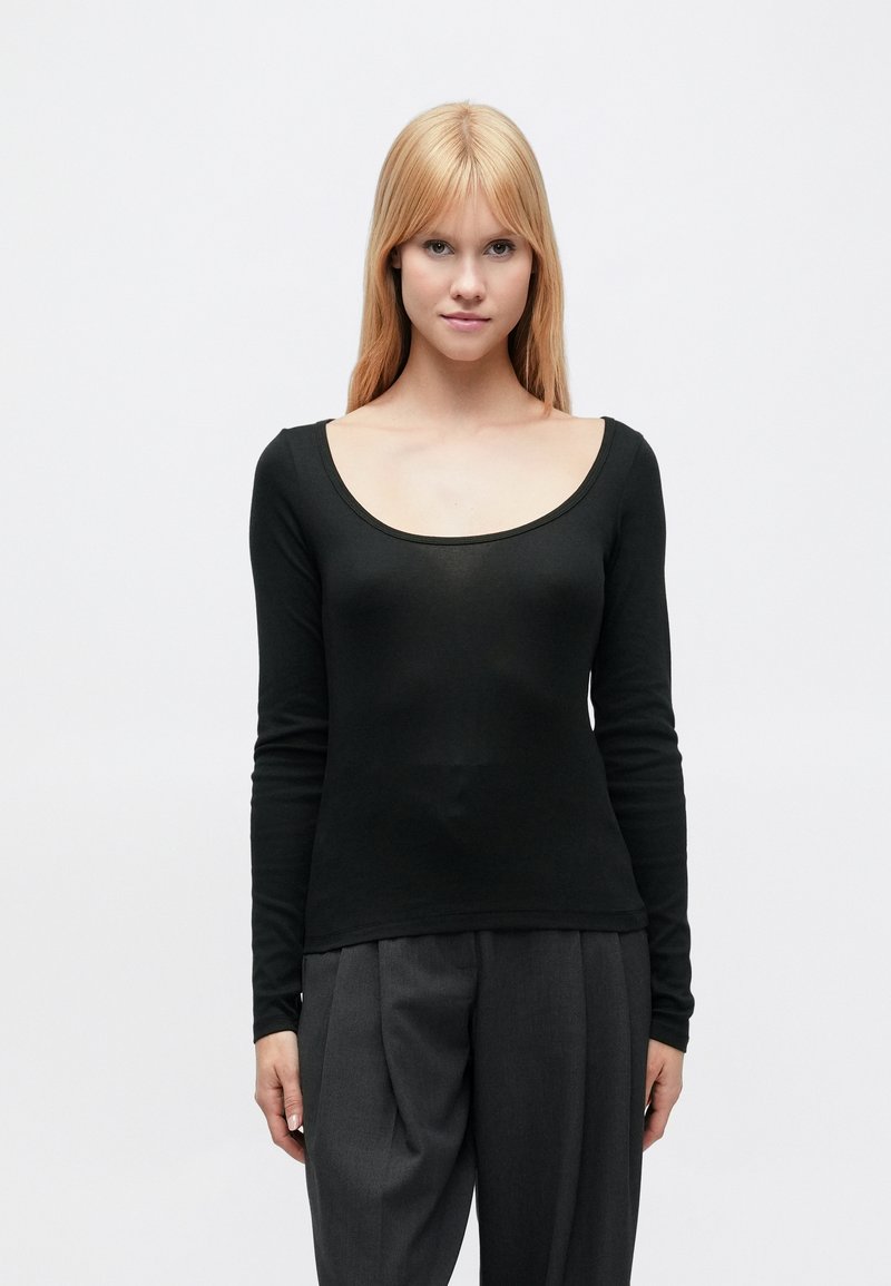 Μαύρο τοπ με μακριά μανίκια και φαρδύ ντεκολτέ σε σχήμα σέσουλας. Απαλή, λεία υφή με εφαρμοστή γραμμή, συνδυασμένο με φαρδιά γκρι παντελόνια.