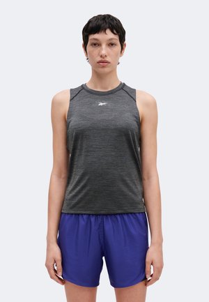 Jeune personne aux cheveux courts et foncés, portant un débardeur de sport gris ainsi qu'un short bleu vif sur un fond clair uni.
