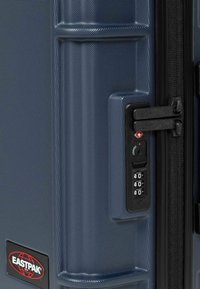 Modrý tvrdý kufr s texturovaným povrchem, kombinovaným zámkem a černými zipovými akcenty. Logo Eastpak je výrazně zobrazeno.