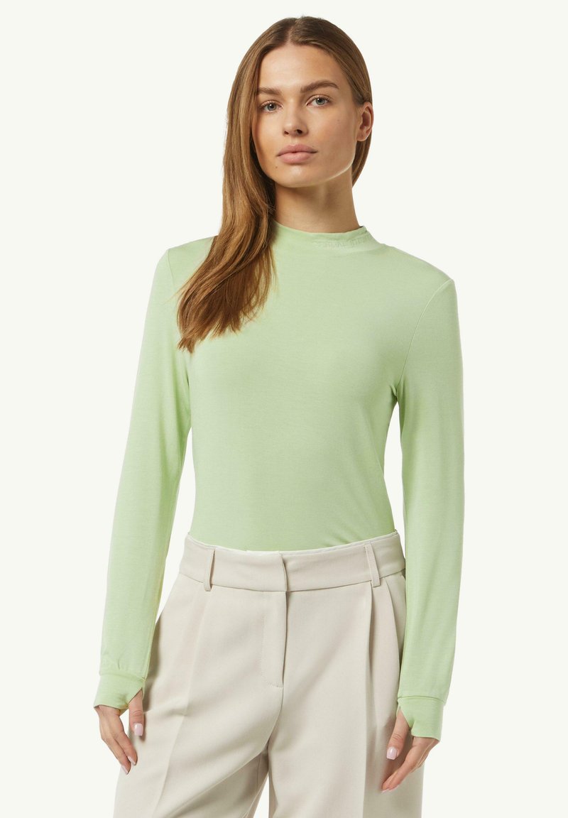 Lichtgroene lange mouwtop met hoge hals en aansluitend ontwerp, gemaakt van zachte stof. Gecombineerd met lichtbeige broek met plooien.