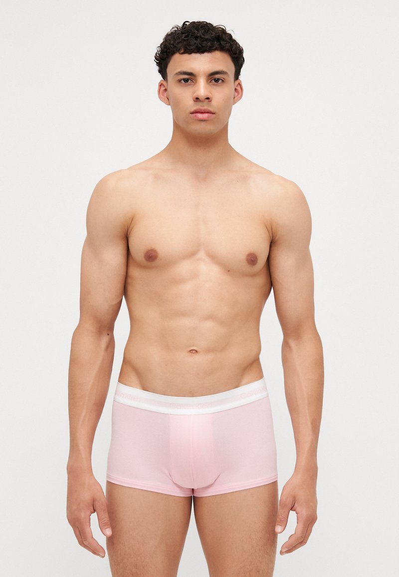 Lichtroze boxershort met een witte elastische band met reliëfbranding. Glad oppervlak en aansluitend ontwerp. Model poseert rechtop.