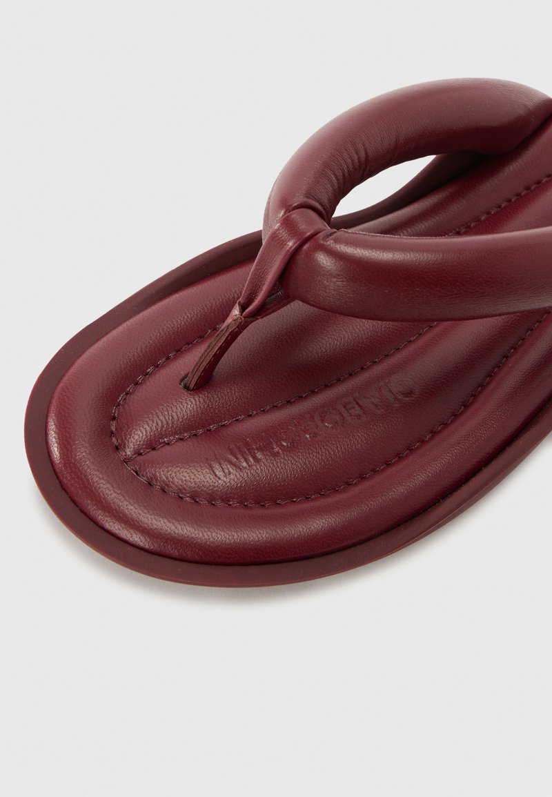 Burgundy leather flip-flop featuring a circular toe post, soft padded footbed, and stitched detailing along the edges for added texture.