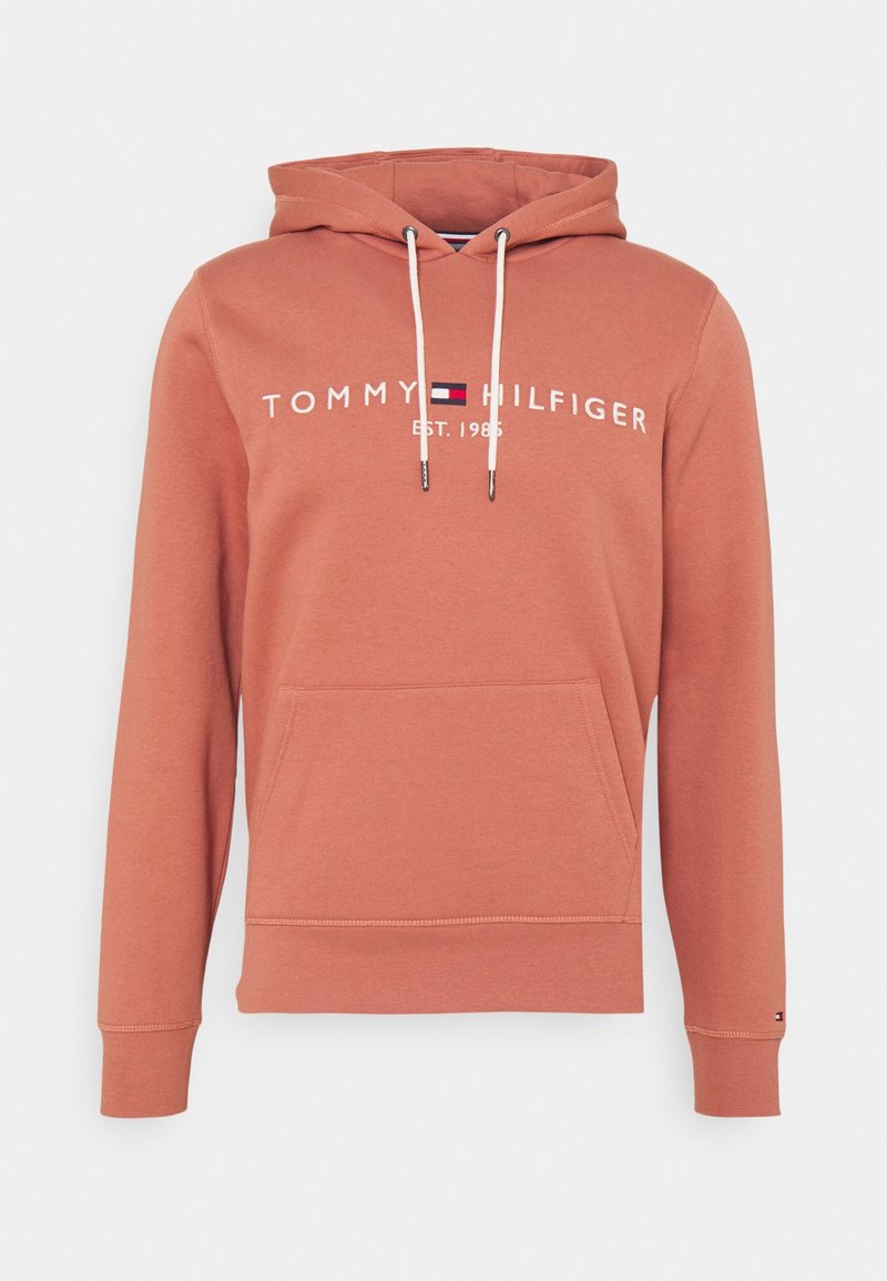 Rust-colored hoodie with front pocket, white drawstrings, and "Tommy Hilfiger Est. 1985" logo in white and navy red on the chest.