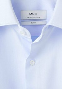 Světlo modra, oprijeta moška srajca s gladko teksturo, z klasičnim ovratnikom in belimi gumbi. Oznaka pravi "MNG THE SUIT COLLECTION."