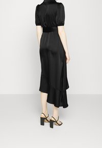 Robe midi en satin noir avec manches courtes bouffantes, taille cintrée et ourlet asymétrique. Associée à des sandales noires à talons carrés.