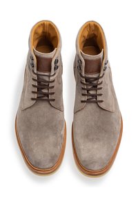 Botines de ante marrón con forro de cuero color marrón claro, puntera redonda, cordones en la parte delantera y ojales marrones con una suela clara en contraste.