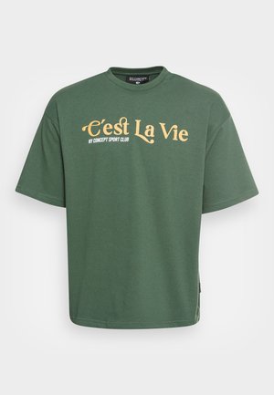 Grünes T-Shirt mit kurzen Ärmeln und gelbem "C'est La Vie" sowie weißem Schriftzug "NY Concept Sport Club" auf der Vorderseite.