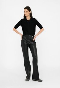 Svart kortärmad stickad topp med krage, kombinerad med högmidjade svarta byxor i konstläder med knappdetalj framtill.