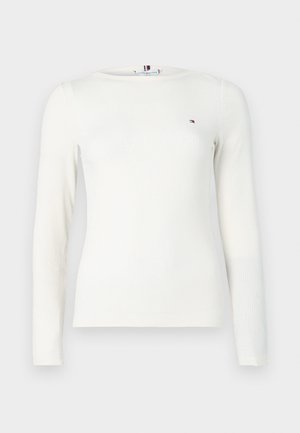 Biely rebrovaný top s dlhým rukávom, okrúhlym výstrihom a malým logom na hrudi. Tkanina sa zdá byť jemná a štruktúrovaná.