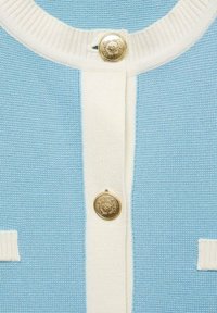 Cárdigan de punto azul claro con detalles en crema, que presenta un cuello acanalado y un botón dorado con un diseño floral en la parte delantera.