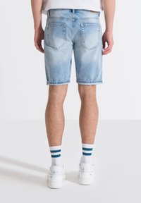 Shorts de mezclilla de color azul claro con un acabado ligeramente desgastado, dobladillos enrollados y dos bolsillos traseros, combinados con zapatillas blancas y calcetines a rayas.