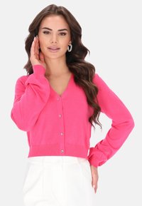 Růžový kardigan s výstřihem do V a dlouhými rukávy, má řadu lesklých knoflíků vpředu a přiléhavý pás v pase. Hladká textura.