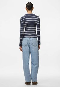 Långärmad marinblå randig topp med vita ränder, kombinerad med ljusblå, löst sittande jeans. Jeansen har två bakfickor och en lätt textur.