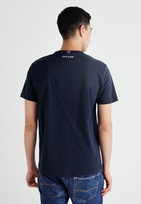 Tamsiai mėlyna medvilninė marškinėlių T-shirt su trumpomis rankovėmis, apvalia iškirpte ir "PEPE JEANS" logotipu ant nugaros, virš dryžuoto akcento.