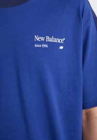 T-shirt bleu à manches courtes en coton doux. Présente un col rond et un texte imprimé blanc : "New Balance depuis 1906" avec logo.