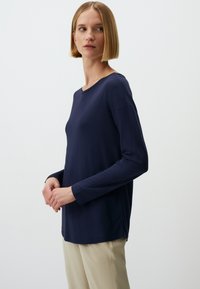 Marineblaues Langarmoberteil mit Rundhalsausschnitt und lockerer Passform, aus glattem Stoff gefertigt, kombiniert mit beigen Hosen.