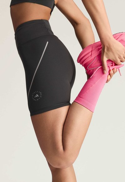 Person stretching leg backward, wearing black athletic shorts, pink socks, and pink running shoes.