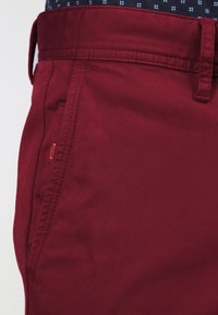 Röda bomullbyxor med slim fit, sidoficka och bältesöglor. Tyget har en slät yta med lätt glans.