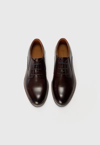 Braune Leder-Schuhe mit glatter Oberfläche, abgerundetem Zehenbereich und Schnürdesign. Sie verfügen über kontrastierende Nähte und ein helles Innenfutter.