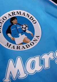 Lichtblauw sportshirt met een geborduurde ronde patch van Diego Maradona, waarop hij met een voetbal staat afgebeeld, met het label "Maradona."