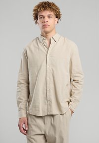 Camicia beige a maniche lunghe con bottoni realizzata in tessuto leggero, dotata di un colletto classico e di una vestibilità rilassata, con bottoni sul davanti.