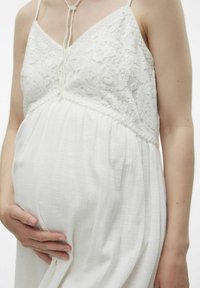 Robe de maternité blanche avec un corsage en dentelle, des bretelles fines et une jupe fluide et plissée. La texture semble lisse et douce.