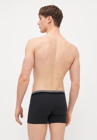 Black boxer briefs with a contrast striped waistband, smooth fabric, and a fitted design, shown from the back on a male model.