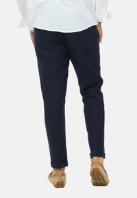 Pantaloni su misura blu navy con vestibilità affusolata, caratterizzati da una texture liscia e orli arrotolati, abbinati a scarpe slip-on color marrone chiaro.